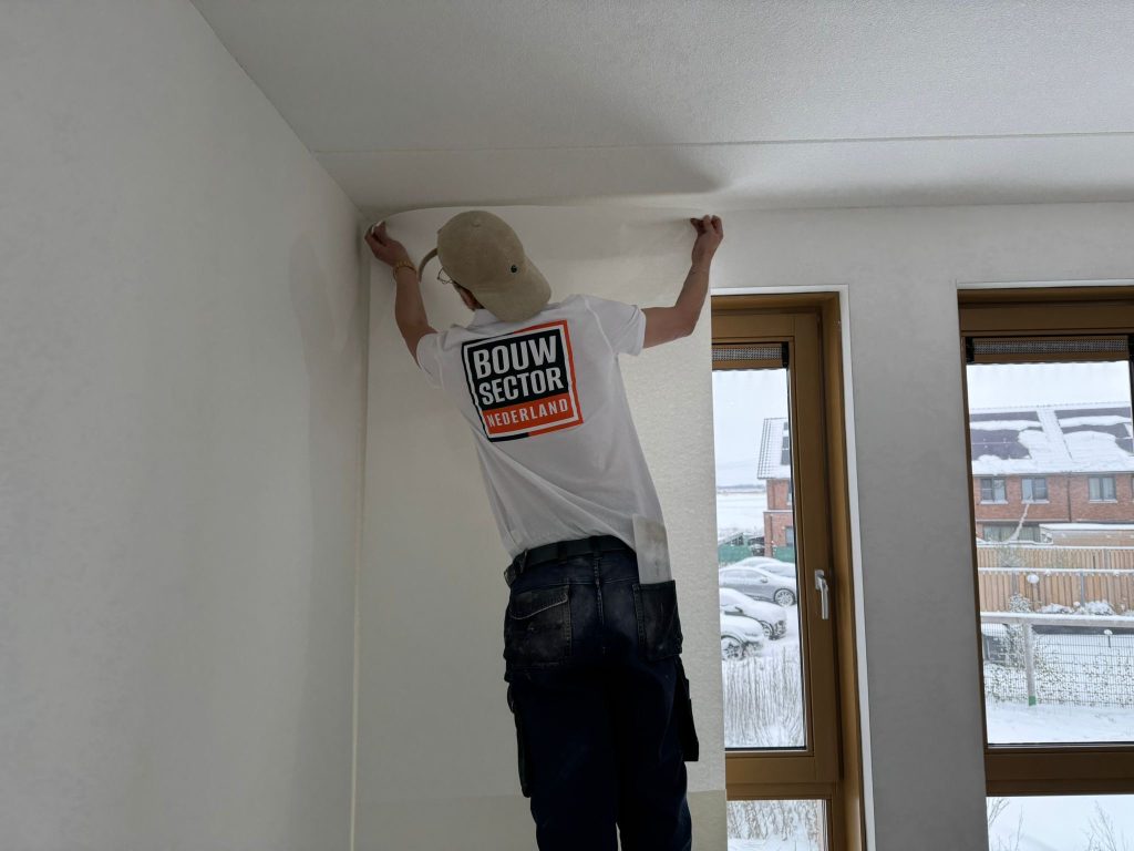 Vakman van Bouwsector Nederland zet een baan vliesbehang strak tegen het plafond