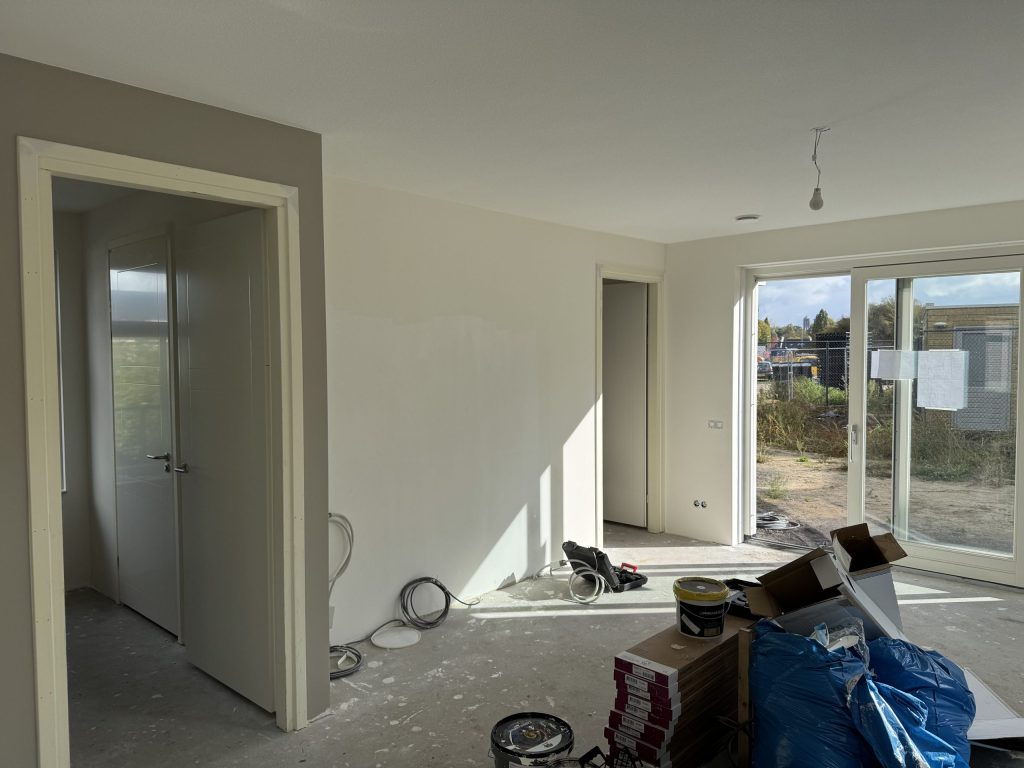 Nieuwbouwwoonkamer tijdens de afwerking, met verfemmers en dozen op de dekvloer