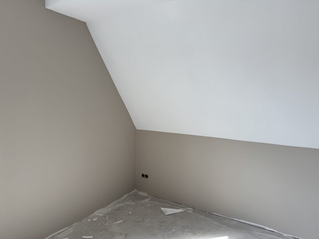 Zolderkamer met een schuine wand onder de kap, net afgewerkt in een zachte beigetint
