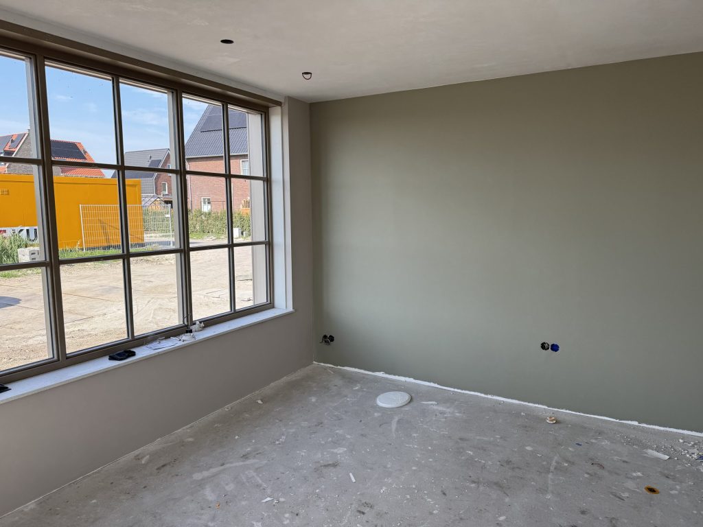 Nieuwbouwkamer met een egaal afgewerkte wand in een grijsgroene tint naast een groot raam